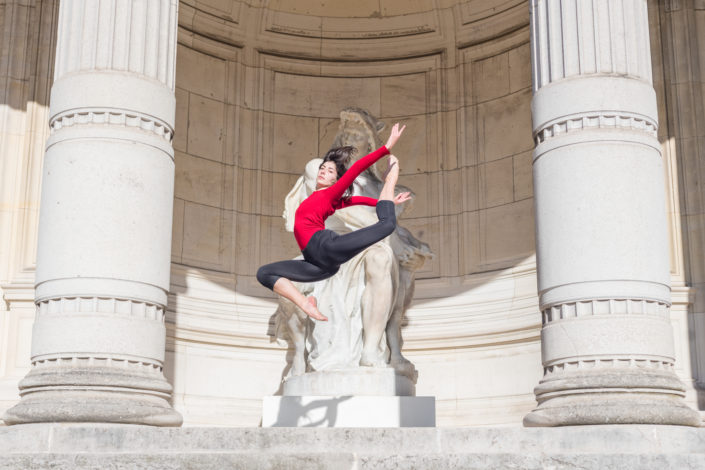 gymnaste faisant un saut avec un justaucorps rouge devant 2 colonnes